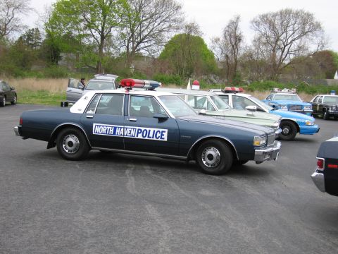 1991 Ford LTD Crown Victoria - dark blue Chevrolet North Haven Police sedan with a single red roof beacon parked among other cruisers.