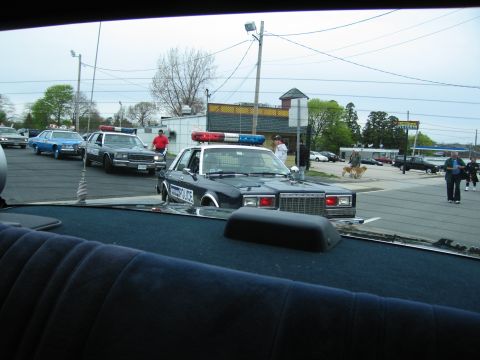 1991 Ford LTD Crown Victoria - black police sedan with roof lights sits in a lot, viewed through the windshield of another vehicle.