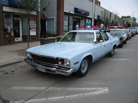1991 Ford LTD Crown Victoria - Front three-quarter view of a light-blue Plymouth Fury State Police sedan parked at the curb among other cruisers.