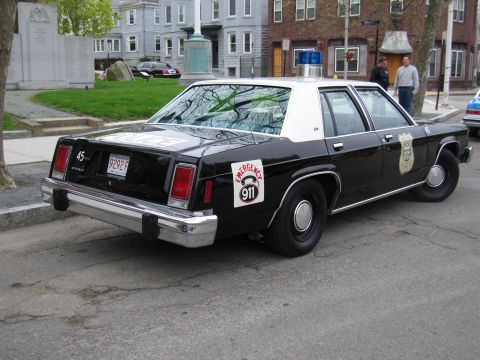 1991 Ford LTD Crown Victoria - Rear three-quarter view of a black-and-white Ford LTD police sedan marked with an Emergency 911 wheel decal.