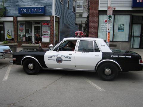1991 Ford LTD Crown Victoria - black-and-white Dodge sedan marked Jaffrey Police Street Crime Unit parked outside Angel Nails on a street.