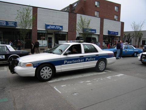 1991 Ford LTD Crown Victoria - white-and-blue Pawtucket Police Ford Crown Victoria cruiser, number 301, driving along a storefront-lined street.