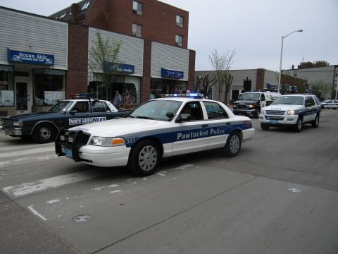 1991 Ford LTD Crown Victoria - white-and-blue Pawtucket Police Crown Victoria leads a line of cruisers including a North Haven car down a street.
