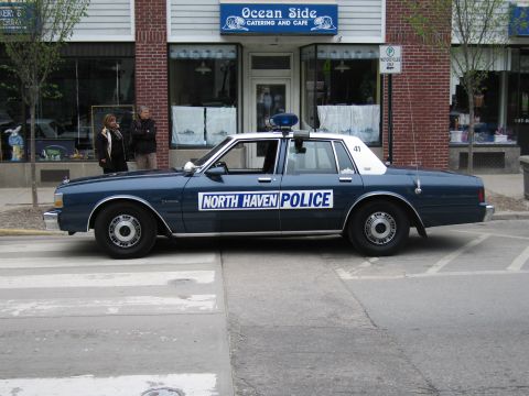1991 Ford LTD Crown Victoria - Side profile of a dark-blue and white North Haven Police sedan with roof beacon parked outside Ocean Side Cafe.