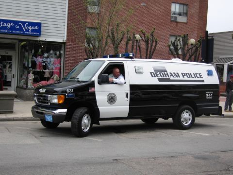 1991 Ford LTD Crown Victoria - black-and-white Dedham Police Ford E-series van, number 631, with an officer at the wheel driving down a street.