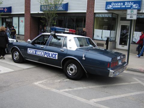 1991 Ford LTD Crown Victoria - Rear three-quarter view of a dark-blue and white North Haven Police sedan with roof lights parked along a street curb.