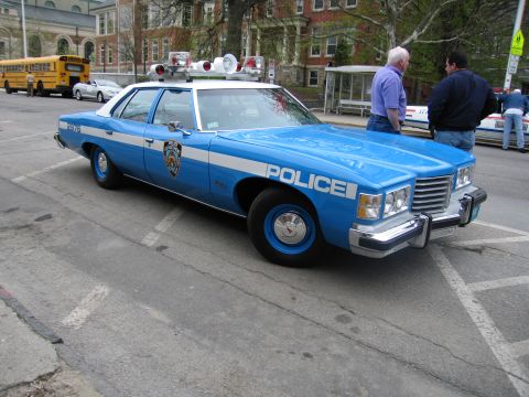 1991 Ford LTD Crown Victoria - blue-and-white NYPD-style Pontiac police sedan with roof beacon and siren parked on a street near a school bus.