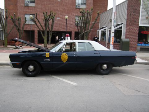 1991 Ford LTD Crown Victoria - Side profile of a dark-blue Plymouth Fury State Police sedan with white roof and open hood parked along a street curb.