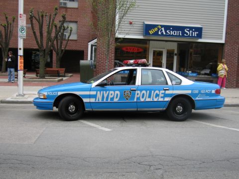 1991 Ford LTD Crown Victoria - Side profile of a blue NYPD Police sedan, unit 1350, parked along a curb in front of the Asian Stir storefront.