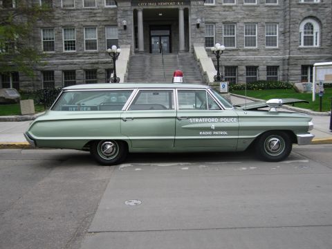 1991 Ford LTD Crown Victoria - vintage green-and-white Stratford Police radio-patrol station wagon parked in front of the stone Newport City Hall building.