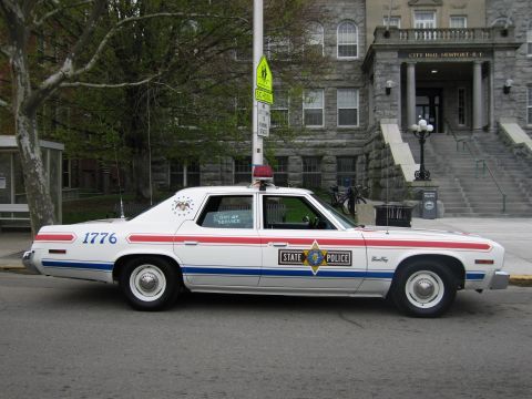 1991 Ford LTD Crown Victoria - white vintage State Police sedan numbered 1776 with red-and-blue striping parked in front of Newport City Hall.