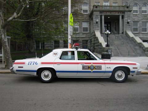 1991 Ford LTD Crown Victoria - Side profile of a white State Police sedan, unit 1776, parked along the curb in front of a stone city hall building.