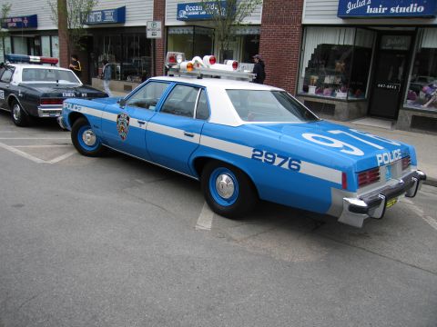 1991 Ford LTD Crown Victoria - Rear three-quarter view of a blue-and-white vintage NYPD Police sedan numbered 2976 parked outside a hair studio.