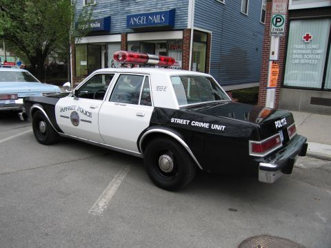 1991 Ford LTD Crown Victoria - Rear view of a black-and-white Jaffrey Police 'Street Crime Unit' sedan parked diagonally on a street near a nail salon.
