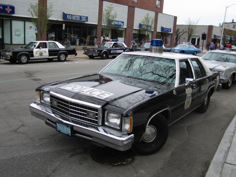 1991 Ford LTD Crown Victoria - Front view of a black-and-white vintage police sedan with 'POLICE' lettered across the hood, parked among other patrol cars.