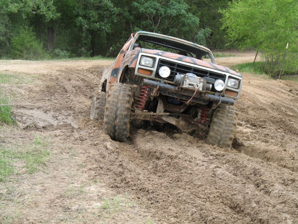 Mud-covered camo off-road truck climbing out of a rutted mud pit