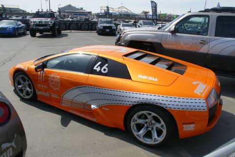 1993 Ford Taurus - An orange sports car with racing decals is parked in a lot with other vehicles.
