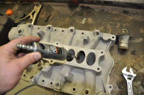 1996 Ford Bronco - A hand uses a rotary tool to modify an intake manifold on a workbench with various tools present.