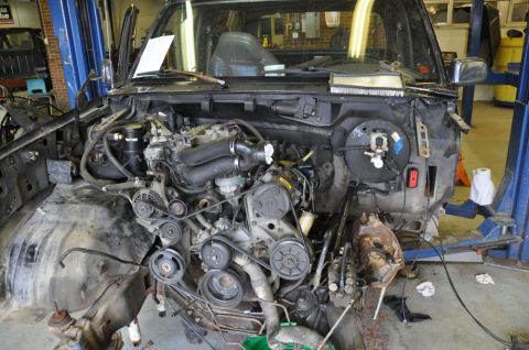 1996 Ford Bronco - Front end of a 1996 Ford Bronco disassembled in a workshop, revealing the engine bay and components.