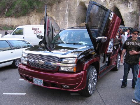 2001 Chevrolet Silverado 1500 - This modified Chevrolet pickup truck features custom butterfly doors and a distinctive grille, parked alongside other vehicles.