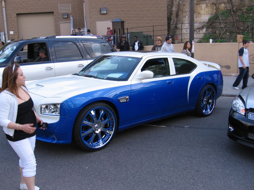 Blue and white car with custom chrome and blue rims parked on street. Another SUV and car visible