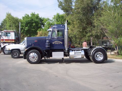 1981 Kenworth W900A - A dark blue semi-truck with "RC WELLS&SON" lettering is parked next to another truck and a white pickup.