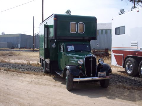1981 Kenworth W900A - A vintage green truck with a custom camper shell is parked next to a white trailer.