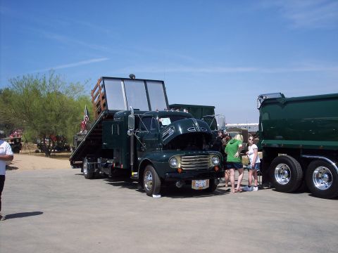 1981 Kenworth W900A - A vintage flatbed truck is displayed with its hood open, alongside a modern dump truck.