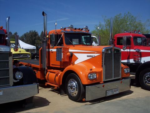 1981 Kenworth W900A - An orange Kenworth truck is parked next to other vehicles under a clear blue sky.