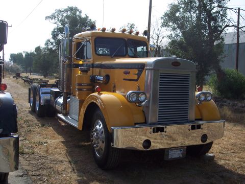 1981 Kenworth W900A - A yellow semi-truck is parked outdoors, with another truck partially visible to its left.