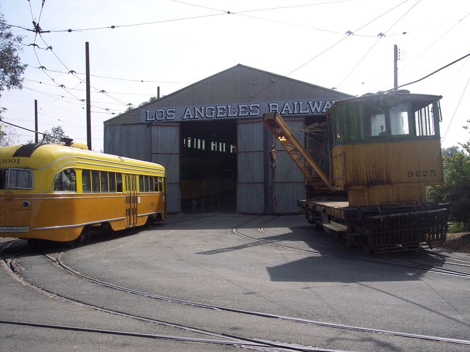 Yellow and orange trolley car and yellow crane truck parked outside Los Angeles Railway building