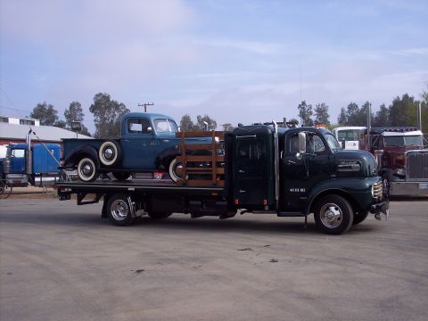 1981 Kenworth W900A - A vintage Mack flatbed truck transports a classic blue pickup truck.