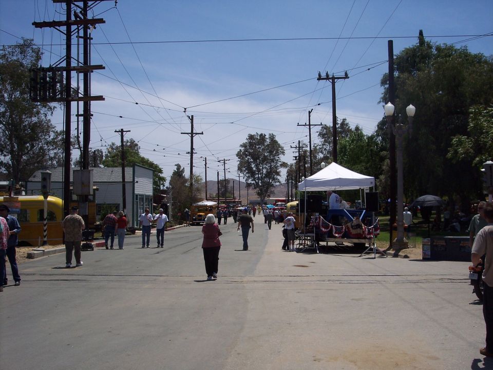Street scene with people walking, utility poles, and a white tent with a stage