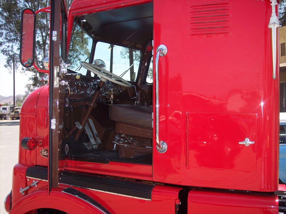 Red semi-truck cab interior with brown seats and steering wheel visible through open door. Exterior door handle and side panel are also shown