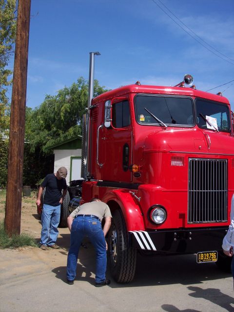 1981 Kenworth W900A - A bright red semi-truck is parked outdoors with two men inspecting its wheels. The truck has a prominent chrome grille and a visible licens…