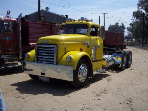 1981 Kenworth W900A - A bright yellow GMC semi-truck is parked on a dirt lot next to a red dump truck.