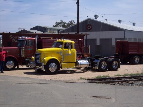 1981 Kenworth W900A - A yellow semi-truck cab is parked in front of a building with other trucks nearby.