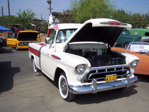 1981 Kenworth W900A - A white 1955 Chevrolet pickup truck with its hood open is parked outdoors next to other vehicles.