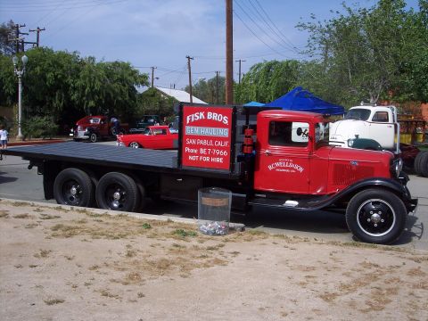 1981 Kenworth W900A - A vintage red flatbed truck is parked next to other classic vehicles under a sunny sky.