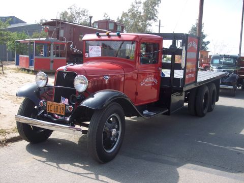1981 Kenworth W900A - A vintage red flatbed truck with "RC WELLSON" lettering on the door is parked on a street, with other vehicles and structures in the backgr…