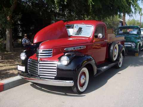 1981 Kenworth W900A - This red 1947 GMC pickup truck is parked next to another truck at an event.