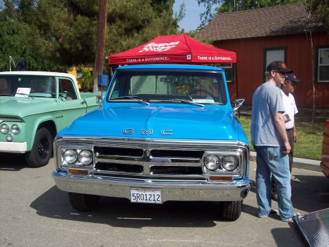 1981 Kenworth W900A - A bright blue GMC pickup truck is parked in front of a red canopy, with another vintage truck visible to the left.