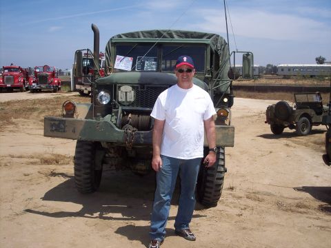 1981 Kenworth W900A - A man stands before a military truck at an outdoor event with other vehicles visible.