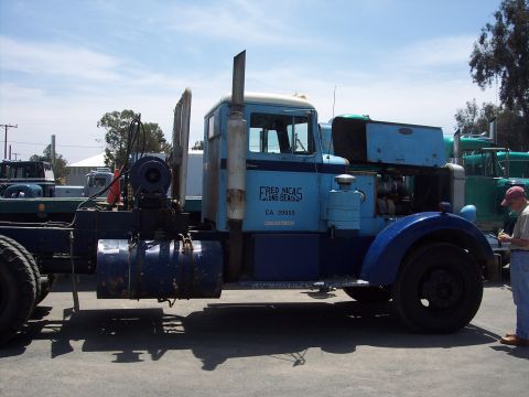 1981 Kenworth W900A - A man inspects a vintage truck, with another truck parked behind it under a sunny sky.