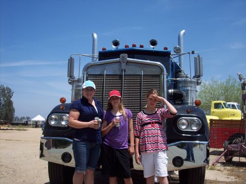 1981 Kenworth W900A - Three people pose in front of a large black semi-truck with a prominent chrome grille.