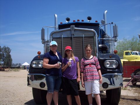 1981 Kenworth W900A - A black semi-truck with a prominent chrome grille is seen from the front, with three people posing in front of it.
