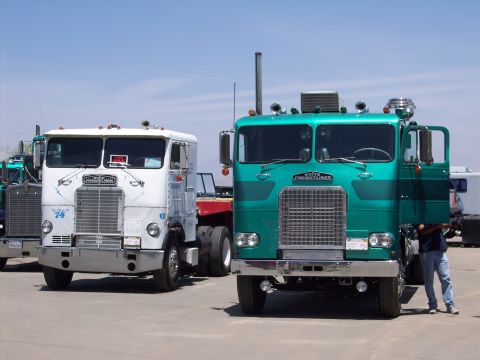 1981 Kenworth W900A - Two semi-trucks are parked outdoors. The truck on the right is teal and has its door open.
