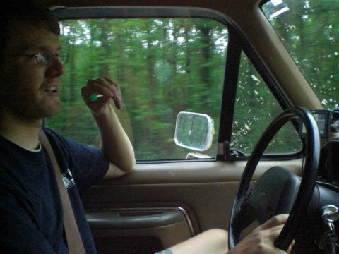 1989 Ford Bronco - A man drives a vehicle through a wooded area, with trees blurring past the window.