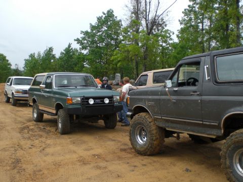 1989 Ford Bronco - Several Ford Broncos are lined up on a dirt path with trees in the background.