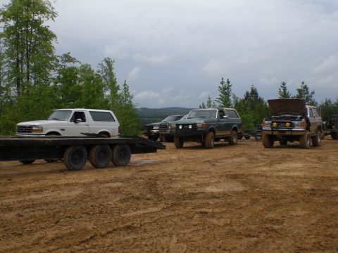 1989 Ford Bronco - Multiple Ford Bronco SUVs are gathered in a muddy field, with one loaded onto a trailer.